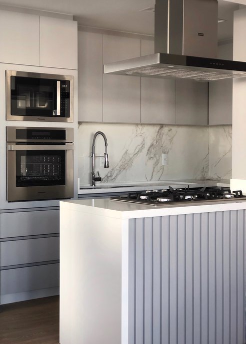 Cada projeto e único e deve refletir a personalidade de quem irá utilizar. Nessa cozinha para um casal com duas crianças e dois cachorros, tudo é funcional e harmônico. O MDF utilizado é com acabamento liso e os puxadores são embutidos, deixando o ambiente clean e moderno. O cinza dos móveis e a bancada em quartzo branco com esse piso vinílico madeirado ficam super aconchegantes. E o detalhe fica por conta do revestimento marmorizado da Portobello 