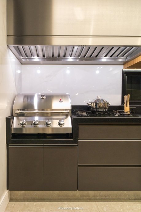 Detalhe da churrasqueira a gás e do cooktop com coifa transformando a cozinha integrada em um verdadeiro espaço gourmet.