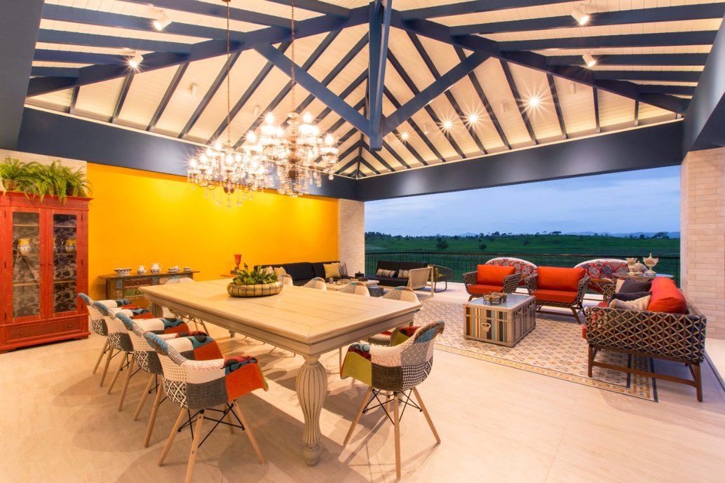 Espaço interno integrado com mesa de jantar, sofás e poltronas, com uma varanda ao fundo com vistas para a fazenda.