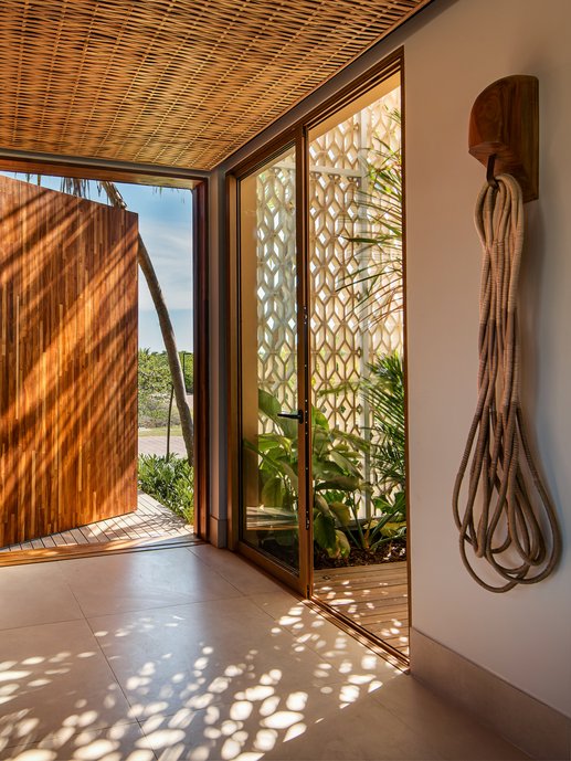 A porta de entrada da residência permite acesso à escadaria que nos conduz ao pavimento superior, que é situada em meio a um jardim interno e banhada pelas sobras do cobogó. 