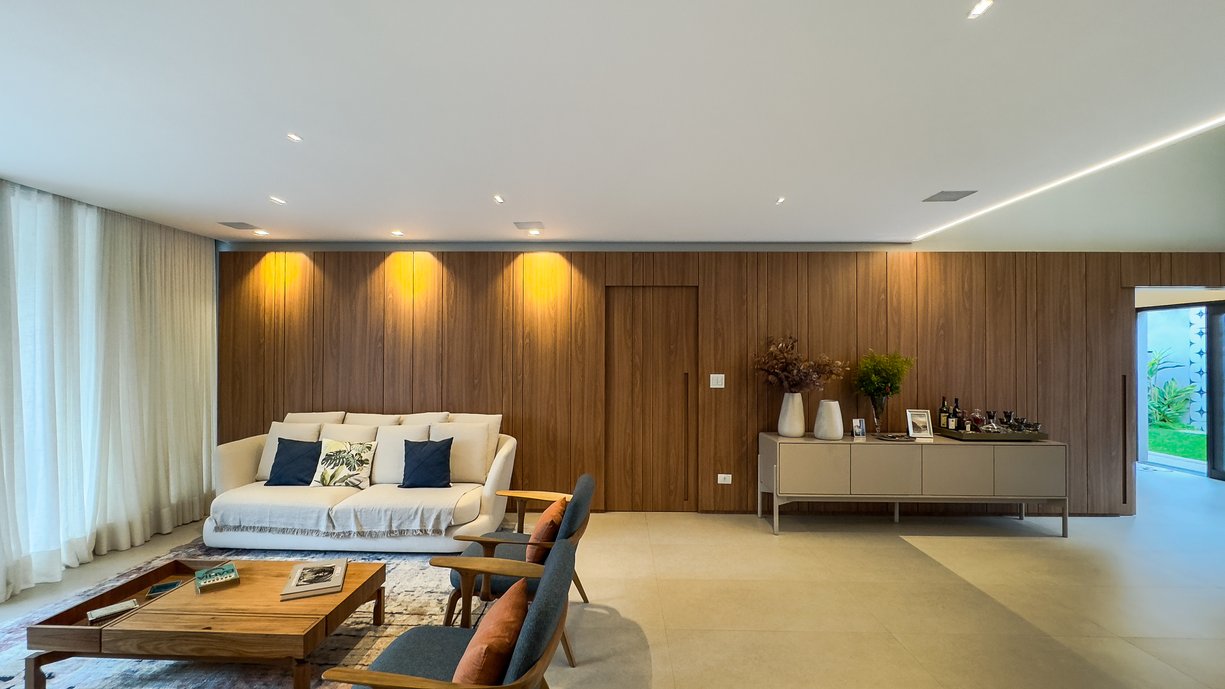 Sala ampla com a composição da madeira nos painéis e o porcelanato claro ampliando os ambientes que se integram 