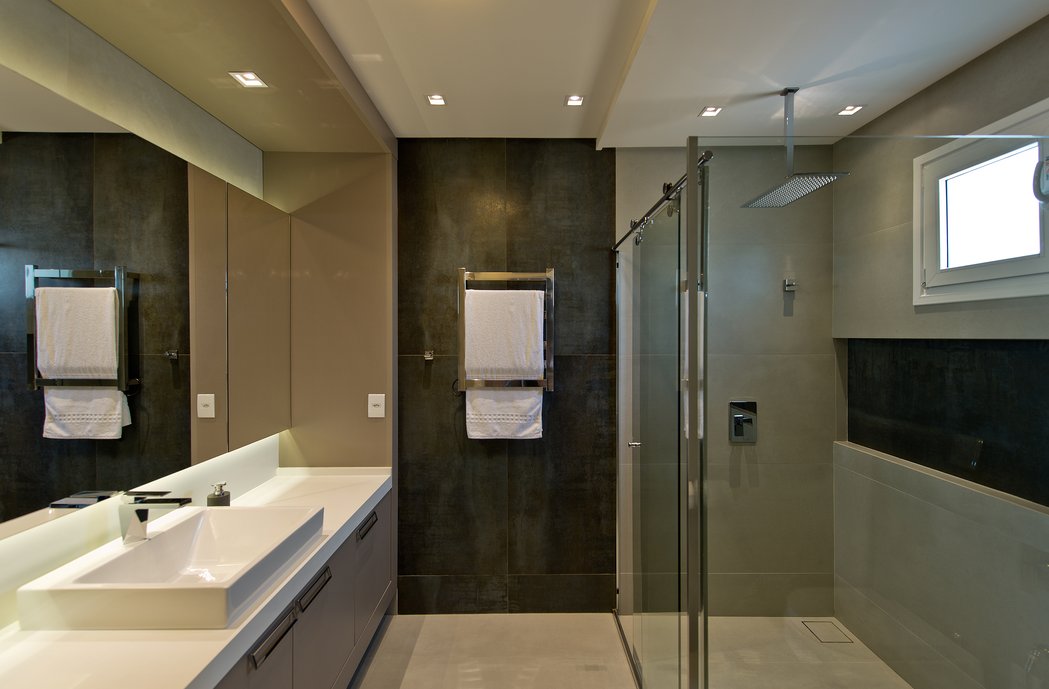 Banheiro masculino em tons escuros, com piso aquecido e toalheiro elétrico.