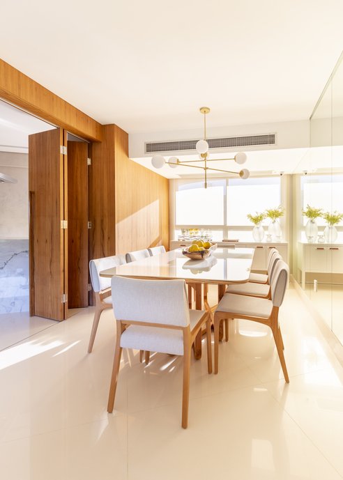 Sala de jantar com piso Portobello Mineral Off White Polido 90x90cm, mesa de jantar Renda (Líder Interiores), cadeiras Anna (Sollos) e esquadria com lâmina de madeira freijó natural.