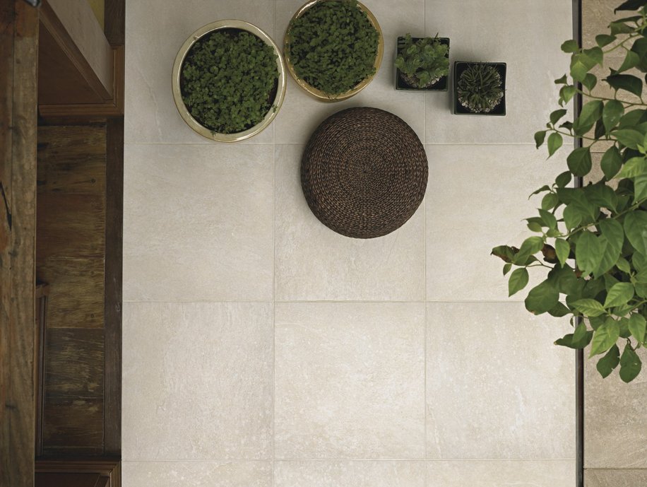 ARPOADOR BIANCO 60X60 NAT BOLD - área externa com vasos de plantas dourados e pufe rústico de palha escura.