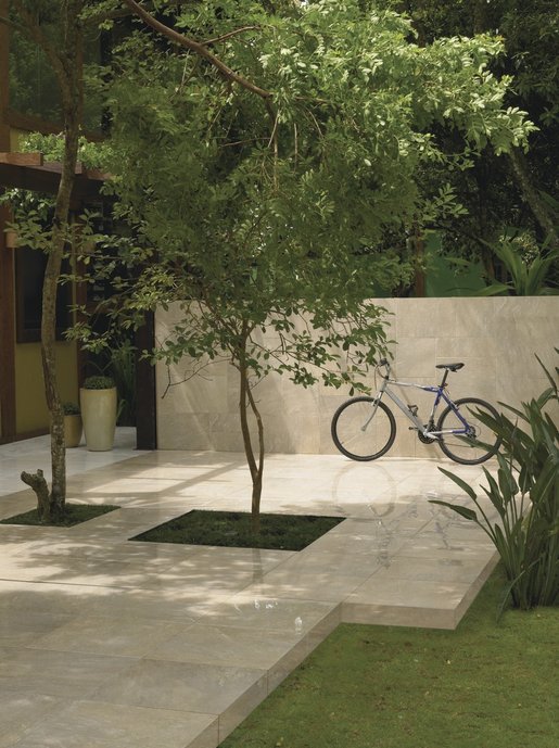 Árvore no jardim da casa e bicicleta encostada na parede da área externa.