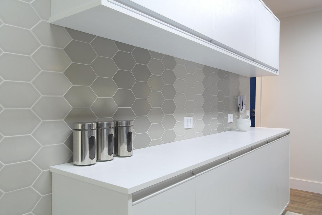 Nas paredes da cozinha americana, o revestimento tem cor discreta, mas ganha movimento e charme por conta do formato hexagonal e da composição com os diferentes tons de cinza.