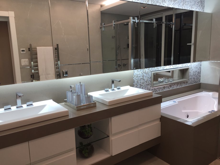 A ?Sala de Banho? é como podemos chamar este espaço contemporâneo, ao mesmo tempo sofisticado e minimalista, foi idealizado pelas arquitetas Liége Pinheiro e Priscila Pinheiro do escritório Ideal Arquitetura de Baln. Camboriú / SC. A aplicação do Revestimento Gris Armani da Portobello traz uma variação do Mármore Bronze Armani em tons prateados com veios levemente cor de ouro, tanto no piso quanto nas paredes. Um clássico no que se refere aos revestimentos de parede! Para realçar ainda mais os diferentes tamanhos que utilizamos dos mesmos produtos, foram aplicados filetes de inox cromados ao longo de toda a parede, combinando com os acabamentos dos metais escolhidos.
Na bancada optamos pelo Silestone Unsui, um clássico dos quartzos, com duas cubas semi encaixadas da Deca e Metais da Linha Dream, uma linha sofisticada, contemporânea e muito versátil, valorizando ainda mais a ?Sala de Banho?.
Vários tipos de iluminação foram aplicados, tanto embutidos nos móveis quanto no forro de gesso. Nesse tipo de iluminação foram usadas lâmpadas que utilizam o teto e as paredes como refletores. A luz produzida é difusa e ideal para suavizar sombras.
Espelhos foram utilizados para ampliar o espaço e também refletir toda a paisagem externa e o skyline da cidade. 