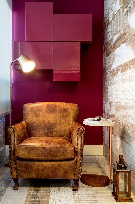 Varanda aconchegante com espaço para leitura e chá da tarde. O ambiente mescla a rusticidade, com o revestimento em porcelanato jacarandá pátina que imita madeira de demolição, com o toque clássico da cômoda e poltrona em couro natural. 