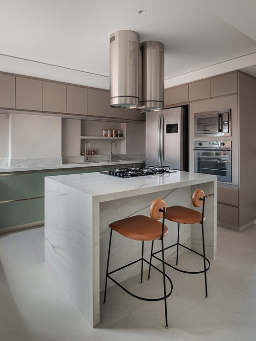 No coração do apartamento, a cozinha foi ampliada, incorporando a antiga área de serviço e ganhando iluminação natural. Esse novo layout permitiu a criação de uma ilha central para o cooktop, além de 