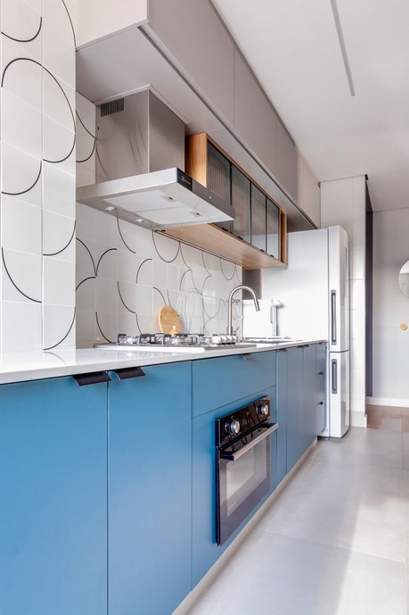 A cozinha integrada à área de serviço conta com o revestimento cheio de personalidade, armários coloridos e, em destaque, uma transição de piso fora do usual para a área social.