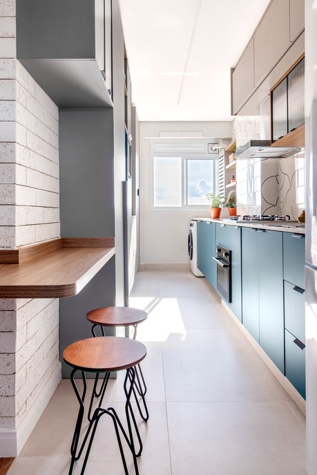 A cozinha integrada à área de serviço conta com o revestimento cheio de personalidade, armários coloridos e, em destaque, uma transição de piso fora do usual para a área social.