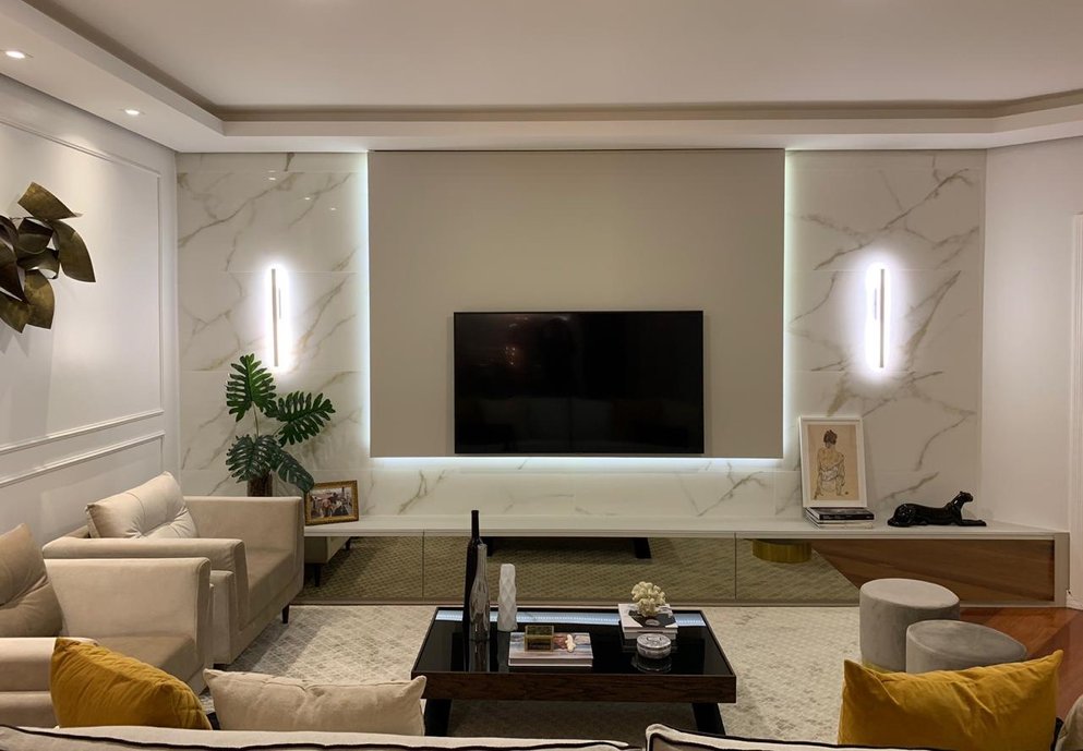 Sala lindissima com painel em porcelanato Oro Bianco polido compondo com marcenaria personalizada e iluminação especial