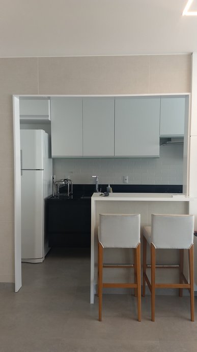 nessa cozinha integrada a sala o porcelanato Superquadra é quem reveste opiso e faz a união dos espaços, e sem soleira para dar mais amplitude. A cozinha tem uma enorme bancada preta que junto ao Liverpool branco traz a modernidade necessária