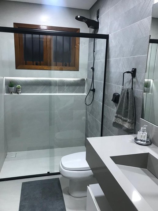 Banheiro social com nicho iluminado, ralo oculto e pia esculpida em silestone e metais pretos