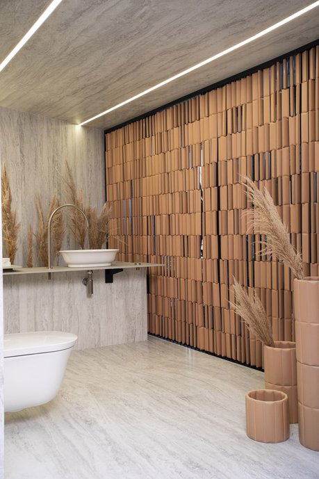 Lavabo - por Patricia Pomerantzeff - O ponto de partida foi a relação das escalas entre as Lastras e o ambiente trabalhado. Usar peças enormes num pequeno lavabo nos provou que a sensação de amplitude é real com o uso das grandes Lastras, sem emendas na altura. Para controlar a entrada de luz e a privacidade do espaço, foi criado um brise usando a linha Biscuit, uma cortina que gera contraste e valoriza ainda mais a grande escala do Travertino Navona Grigio. O Travertino instalado tanto no piso, quanto no forro do lavabo, dessa vez sem recortes, mostra mais uma vez como as possibilidades são ilimitadas para o uso das grandes Lastras.