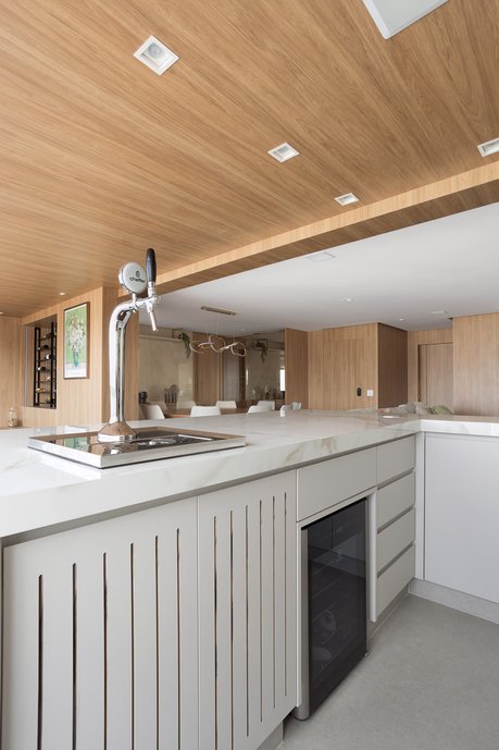 Cozinha gourmet com chopeira embutida, ilha em porcelanato, adega climatizada, marcenaria planejada e teto amadeirado. O ambiente integrado combina design contemporâneo, acabamentos de alto padrão e soluções funcionais para receber amigos e família. Inspiração de arquitetura e design de interiores para cozinhas modernas, áreas gourmet e espaços integrados.