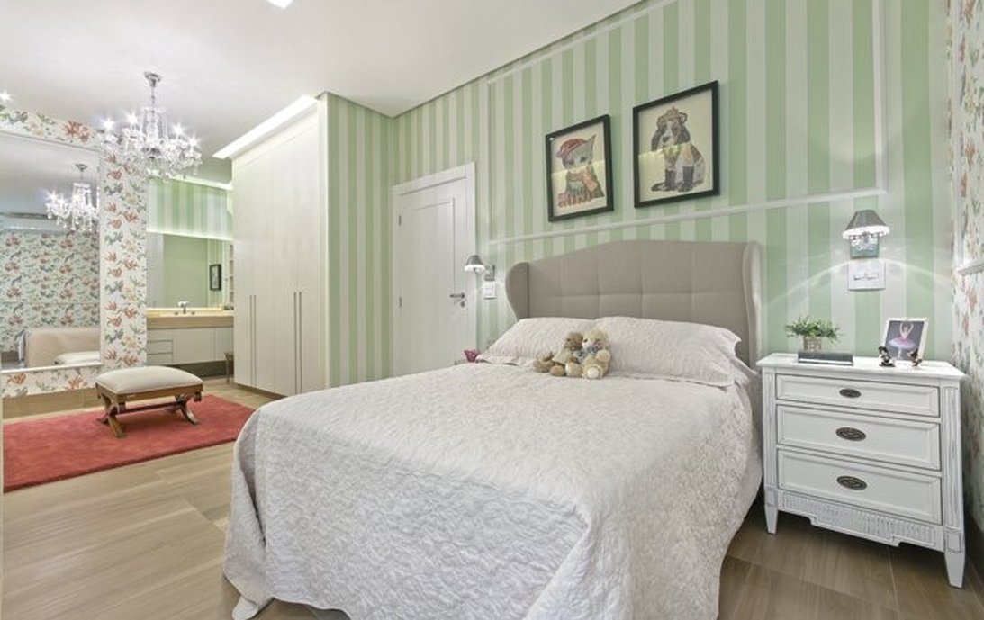 A suite da filha traz composê de papel de parede floral com listrado compondo perfeitamente com as réguas em madeira e a delicadeza do estilo classico.