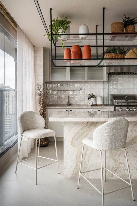 Cozinha gourmet com ilha em pedra natural, marcenaria em madeira e prateleira metálica suspensa. Leveza, textura e integração para receber com estilo.