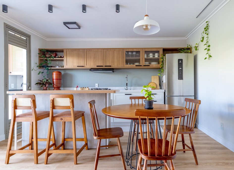 A cozinha, por sua vez, conta com uma ilha central e uma extensa bancada ao longo da parede, onde foram organizados os eletrodomésticos de maneira funcional.