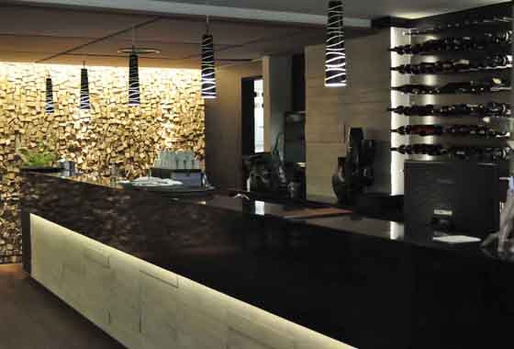 Balcão do bar do restaurante revestido com porcelanato iluminado com fita de led reforçando o relevo das peças