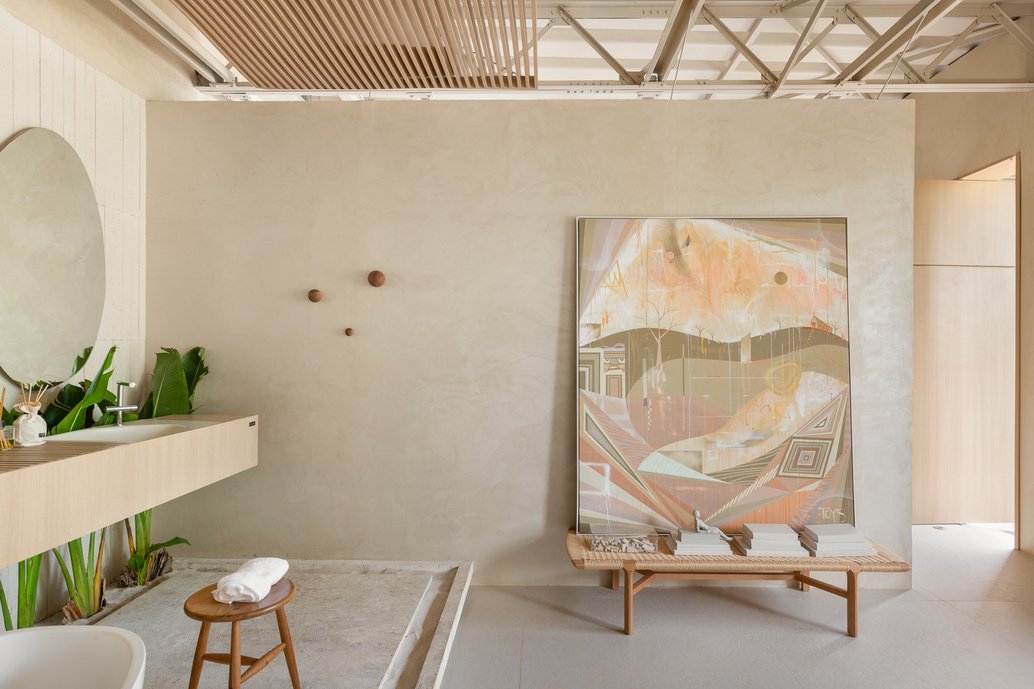 Visual do quarto integrado com lavatório, com banco e tela do artista Daniel Toys